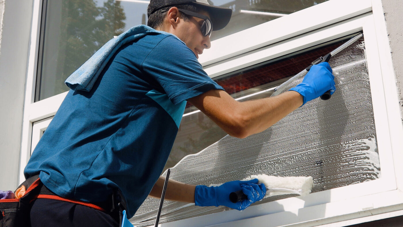 An employee of a professional cleaning service in overalls washes the glass of the windows of the facade of the building. Showcase cleaning for shops and businesses.